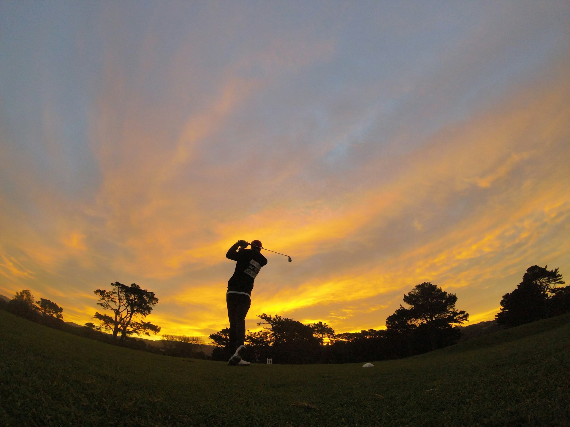 A golfer silhouetted mid-swing against the last light of the day.